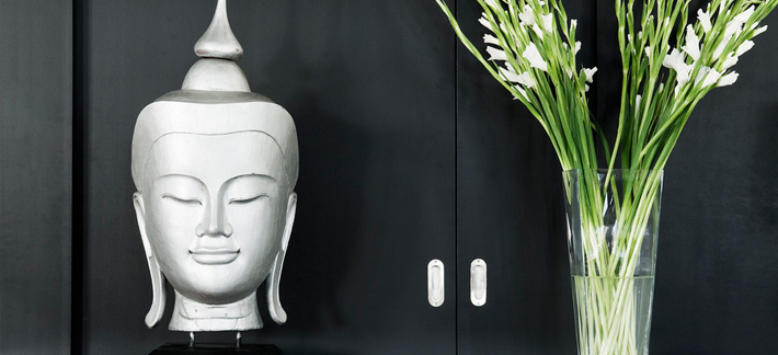 A still life of a light decorative head sculpture beside a glass vase of white flowers, suggesting quiet reflection